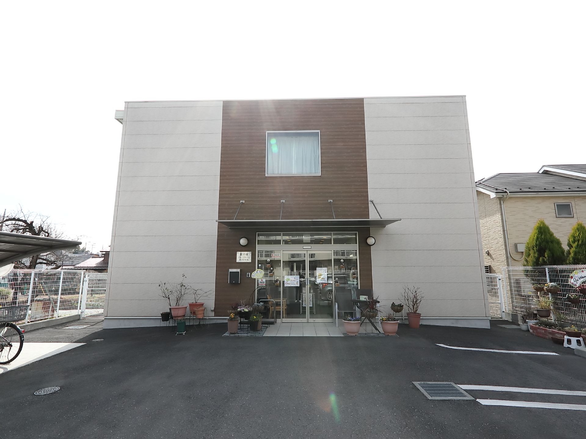 四角形の外観が印象的な２階建てのグループホームである。入り口には自動ドアが完備されている。エントランスには屋根もある。