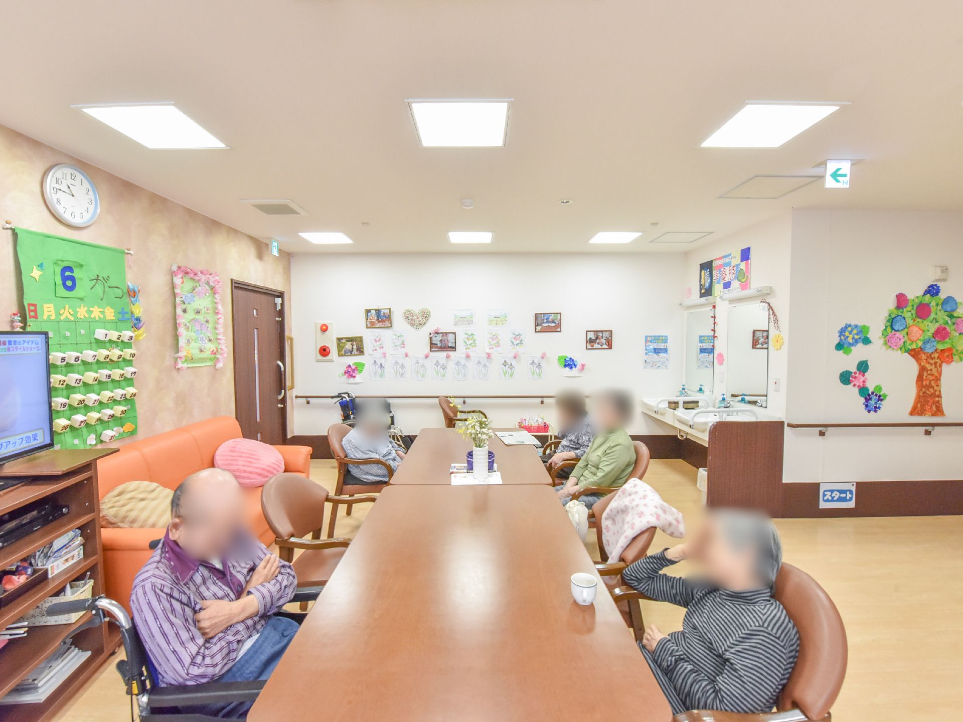 壁面には利用者が作ったレクリエーションの作品などが飾られている。テレビの前で皆それぞれくつろいでいる。