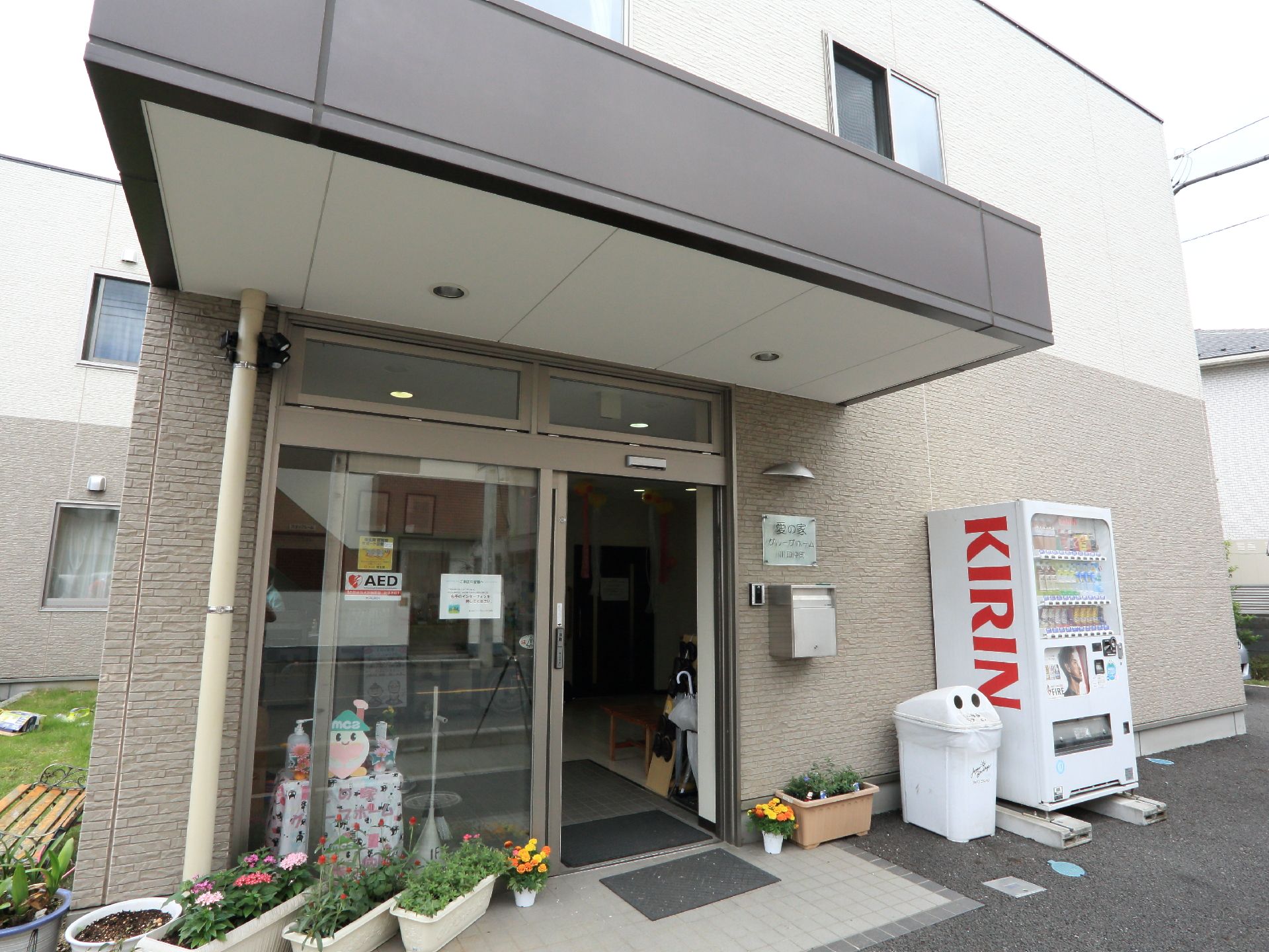 出入り口の前には植物が植えられたプランターが置かれている。外の壁の前には飲み物の自動販売機が設置してある。