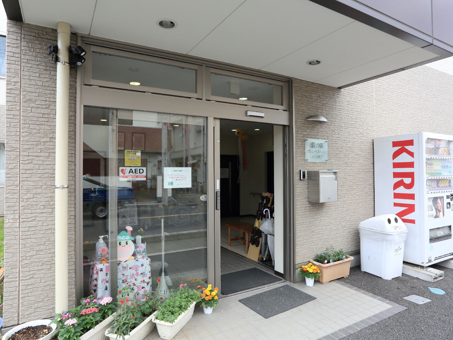 自動ドアの右側、郵便ポストの上には施設名が書かれたおしゃれなガラスプレートが掲げられている。並べられているプランターの花が目をひく。