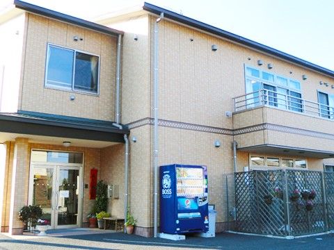 自動販売機の設置された薄いブラウンの外壁の２階建ての建物