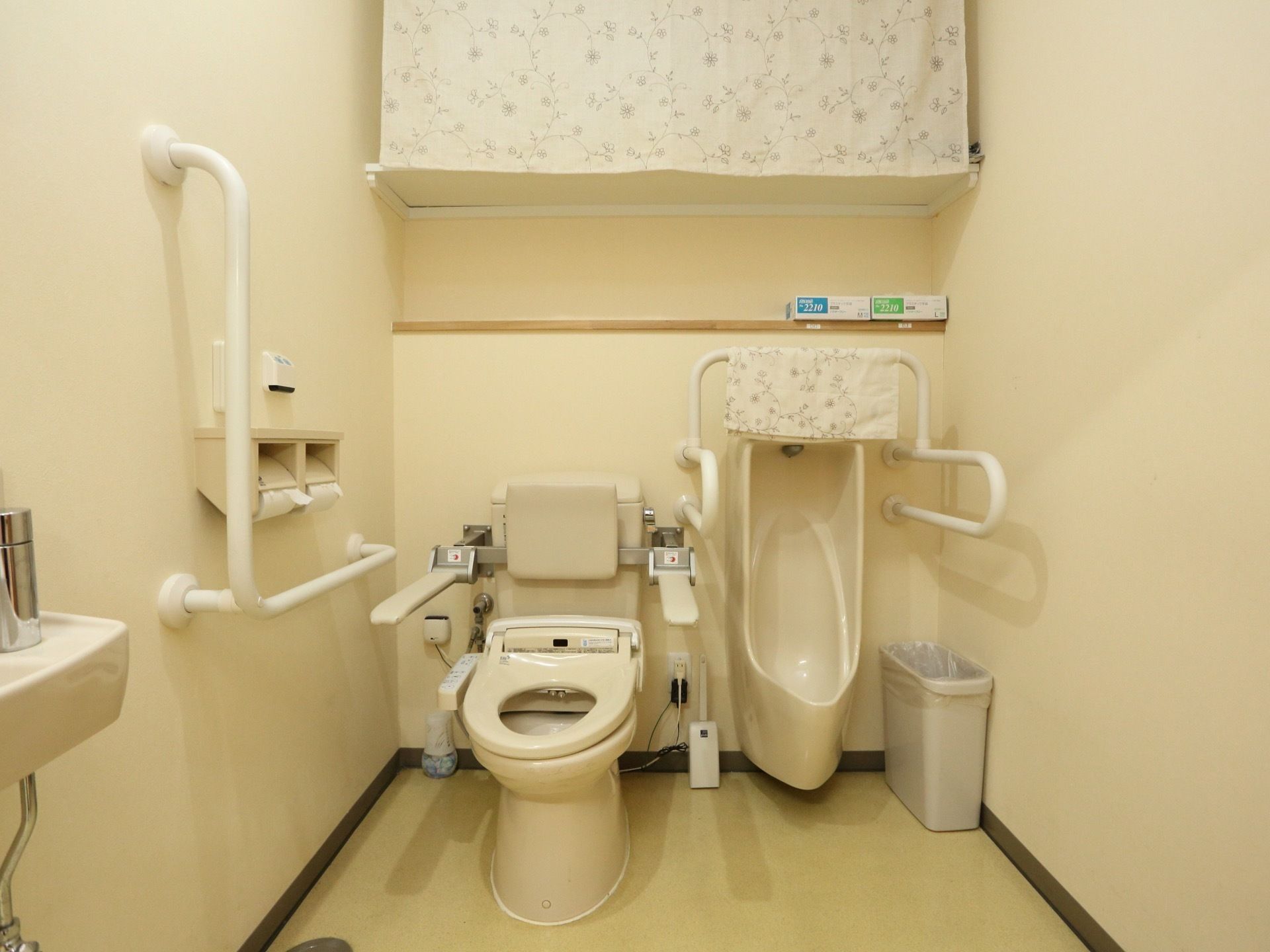ゆったりとした空間に造られた共有トイレは、男性用と男女共有の介護用便座が設置され、壁には手すりとナースコールを配備し安全対策も施されている。