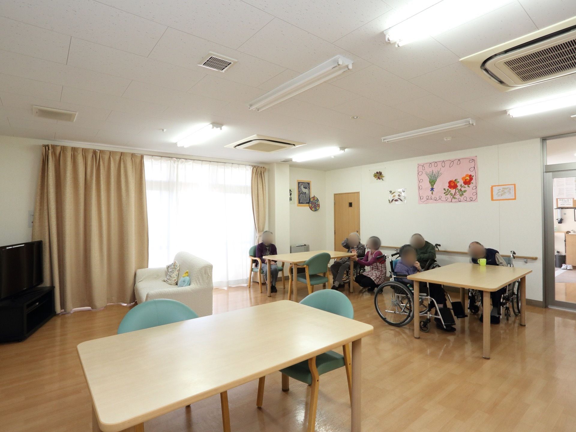 家庭的な雰囲気のリビングでは、入居者様同士テーブルを囲み談笑をして楽しく過ごしている。また、テレビコーナーもありソファーが用意されている。