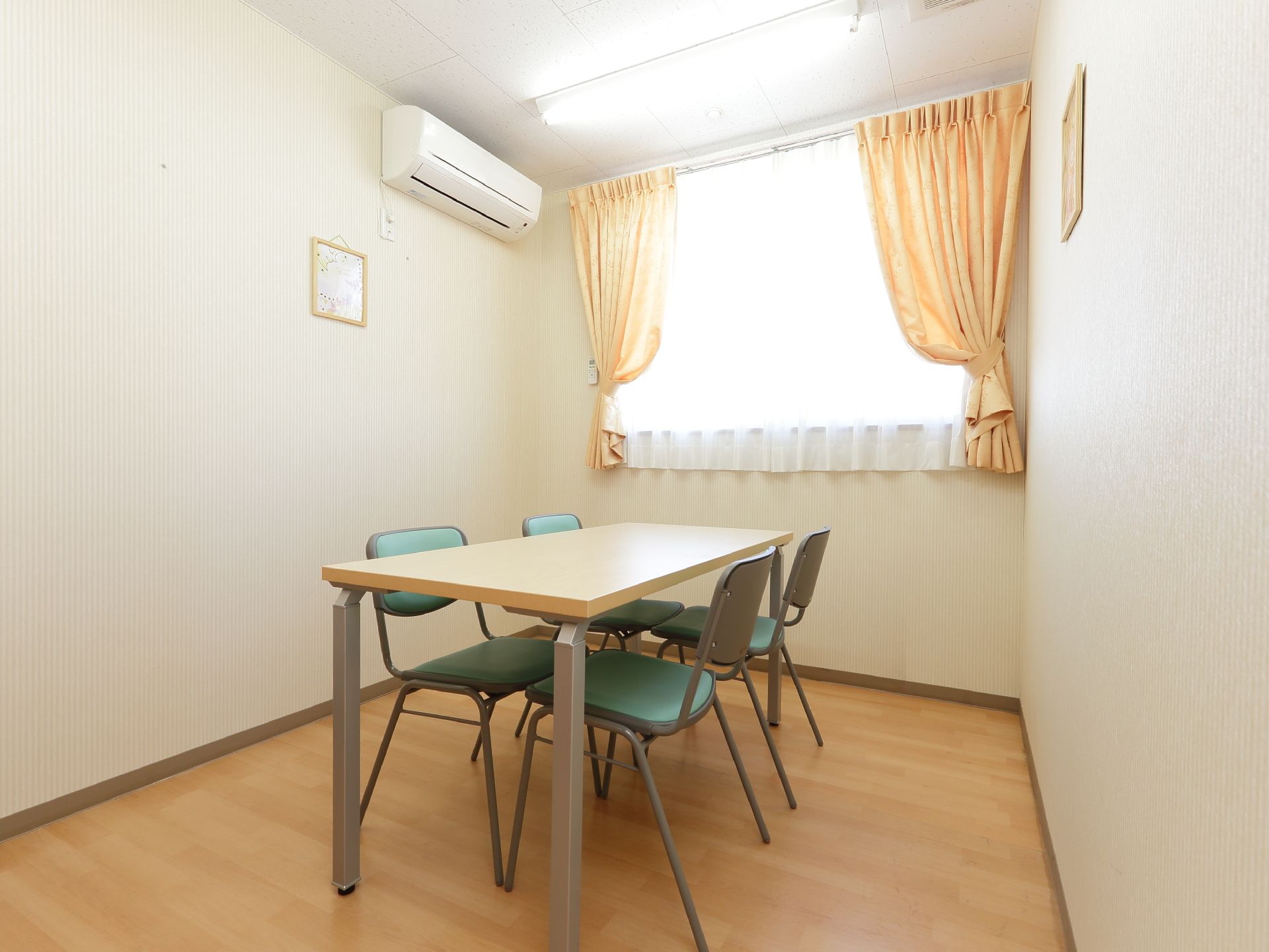 テーブルと椅子が置かれている個室である。腰高窓にはクリームイエローのカーテンが掛けられており、エアコンが設置されている。