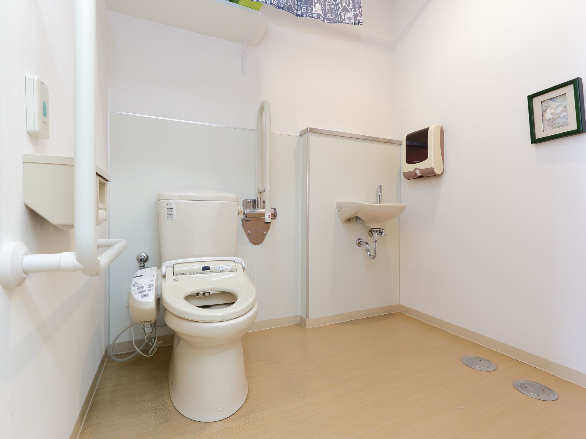 トイレには壁面に手すりが設けられている。同じ空間に手洗い場があり、手をふく紙が壁面に設置されている。