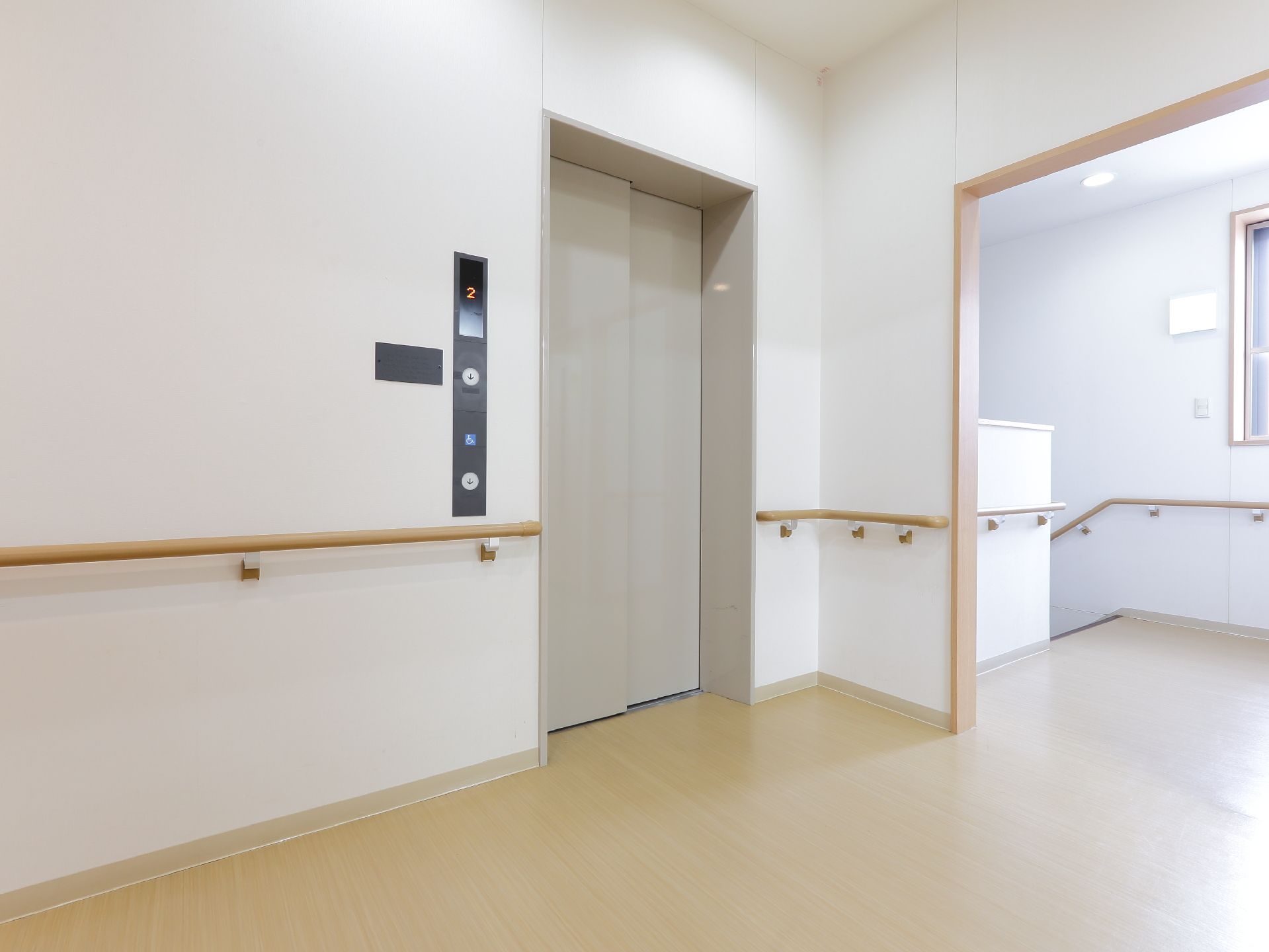 階段横にはエレベーターが設置されている。車いす用のボタンがついている。壁には手すりが設けられている。