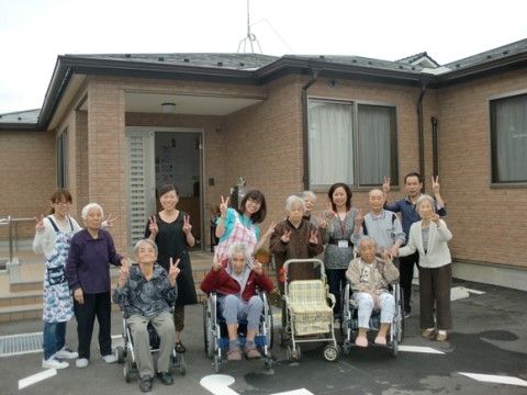 建物の玄関の前でピースサインで記念撮影をする13名の男女