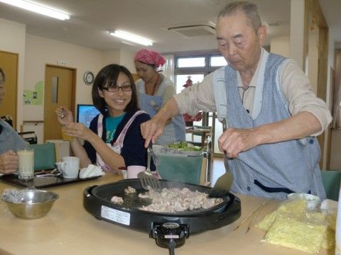ホットプレートに向かって両手にフライ返しを構えるシニア男性