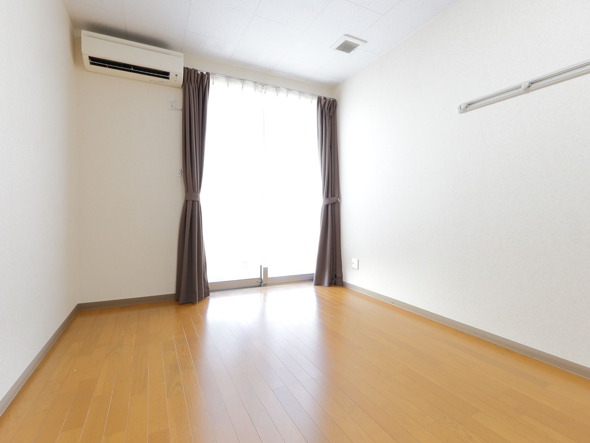 居室の壁には空調設備が備え付けられている。また室内には窓があり、レースカーテンと遮光カーテンが取り付けられている。