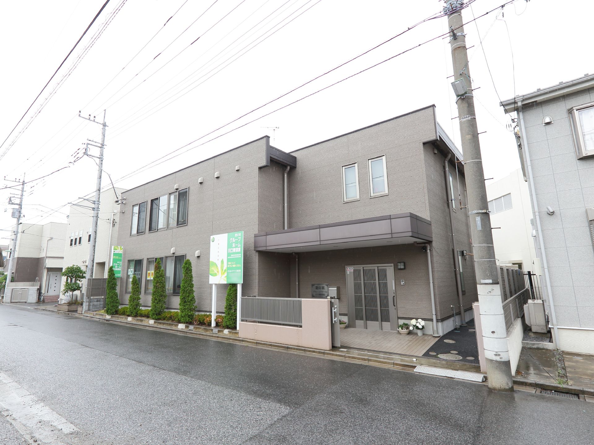 外観はグレーのシンプルな建物である。道路に面している。建物の前には数本木が植えられている。左右には建物が建っている。