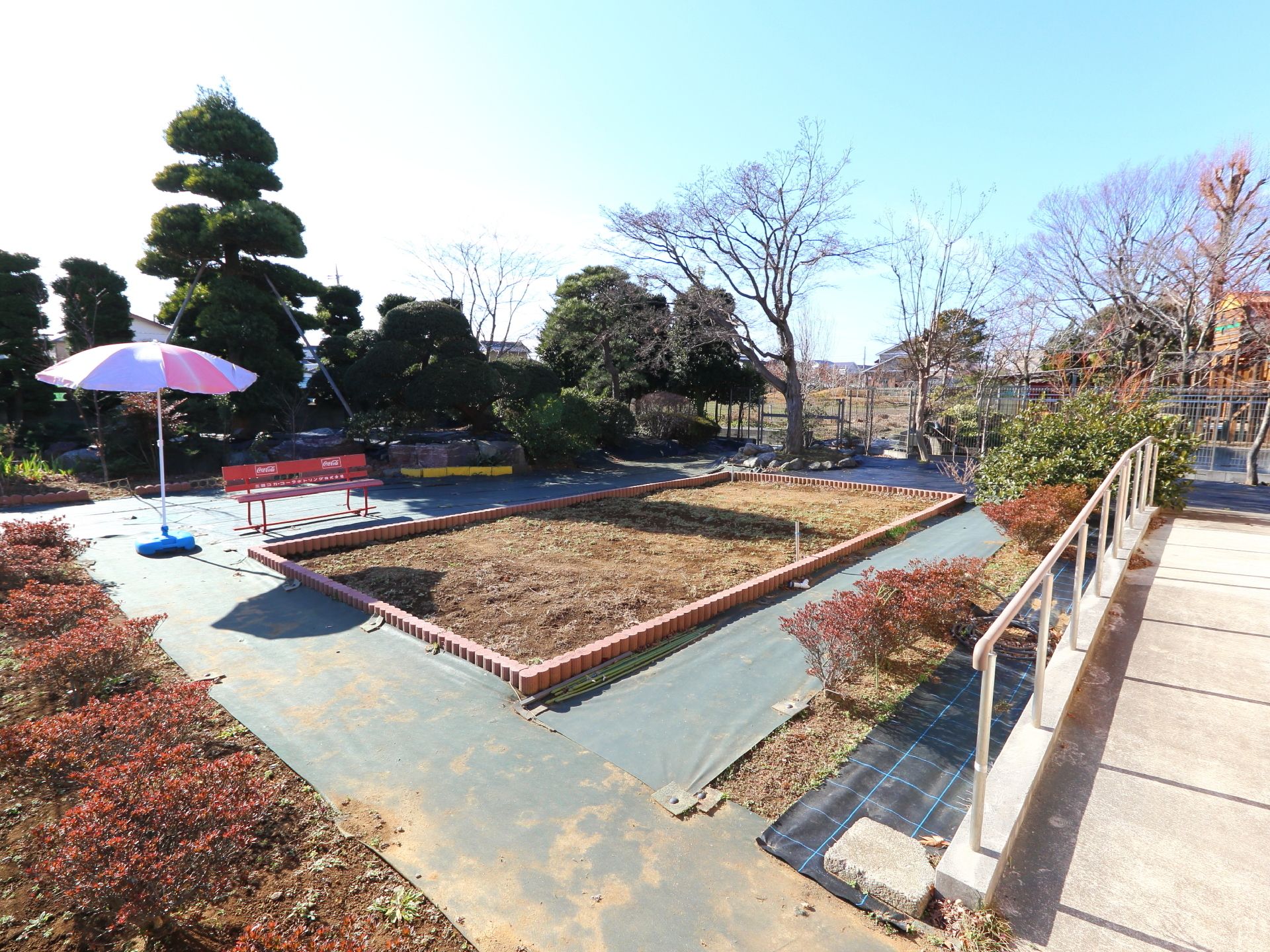 外には植物が植えれるような何もない花壇がある。ベンチが設置されている。パラソルも置かれている。周りにも植物が植わっている。