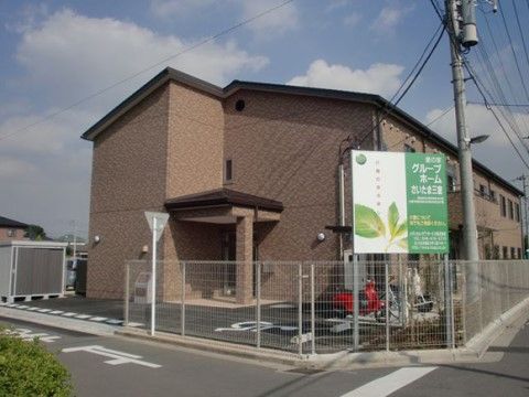茶色い壁のホームには、２階部分にベランダがついた部屋がある。ドア前の駐車場には、車やバイクなどが置ける。