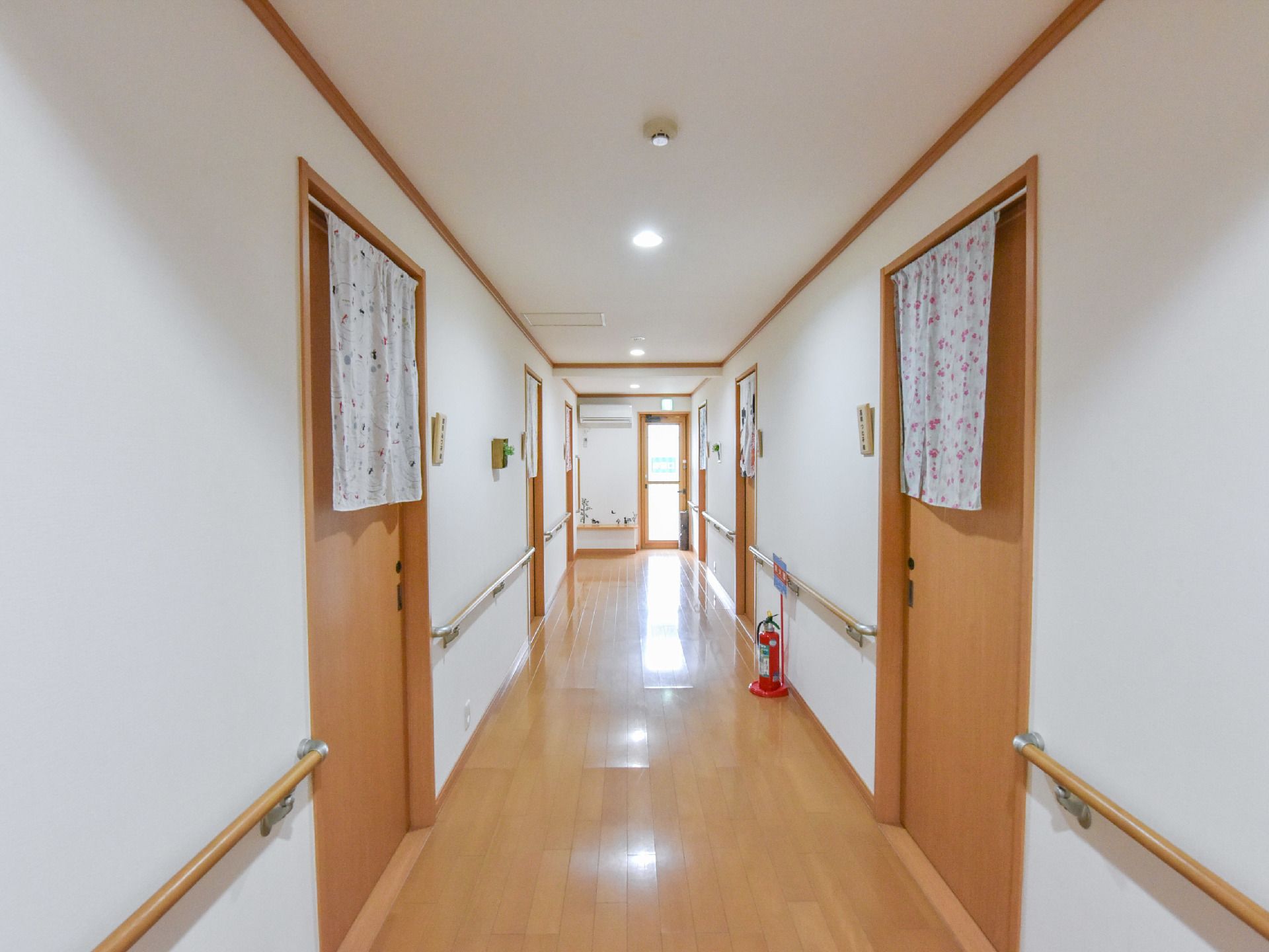 各居室をつなぐ共有廊下。手すりが設置され、居室の引き戸には目の高さに出入りに邪魔にならないのれんが目隠しにかけられている。