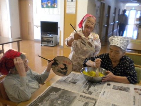 テーブルを囲み二人に団扇で仰がれながらボールの中身を混ぜる女性