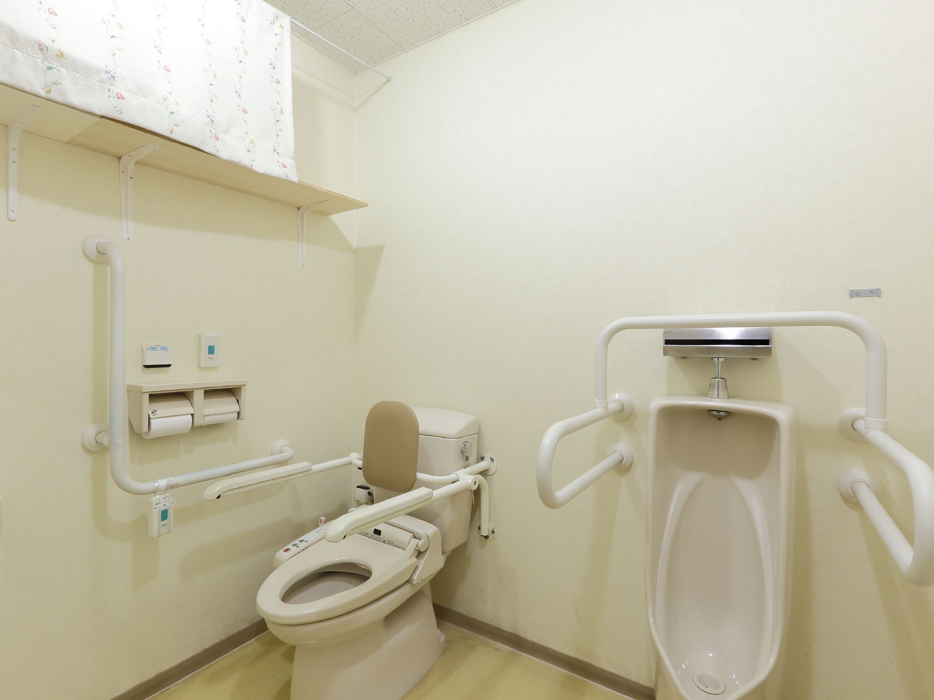 洋式便座と男性用便座が備わったトイレスペース。便座の両脇には手すりが備わっており、立ち座りを補助してくれる。呼び出しボタンが備わっている。