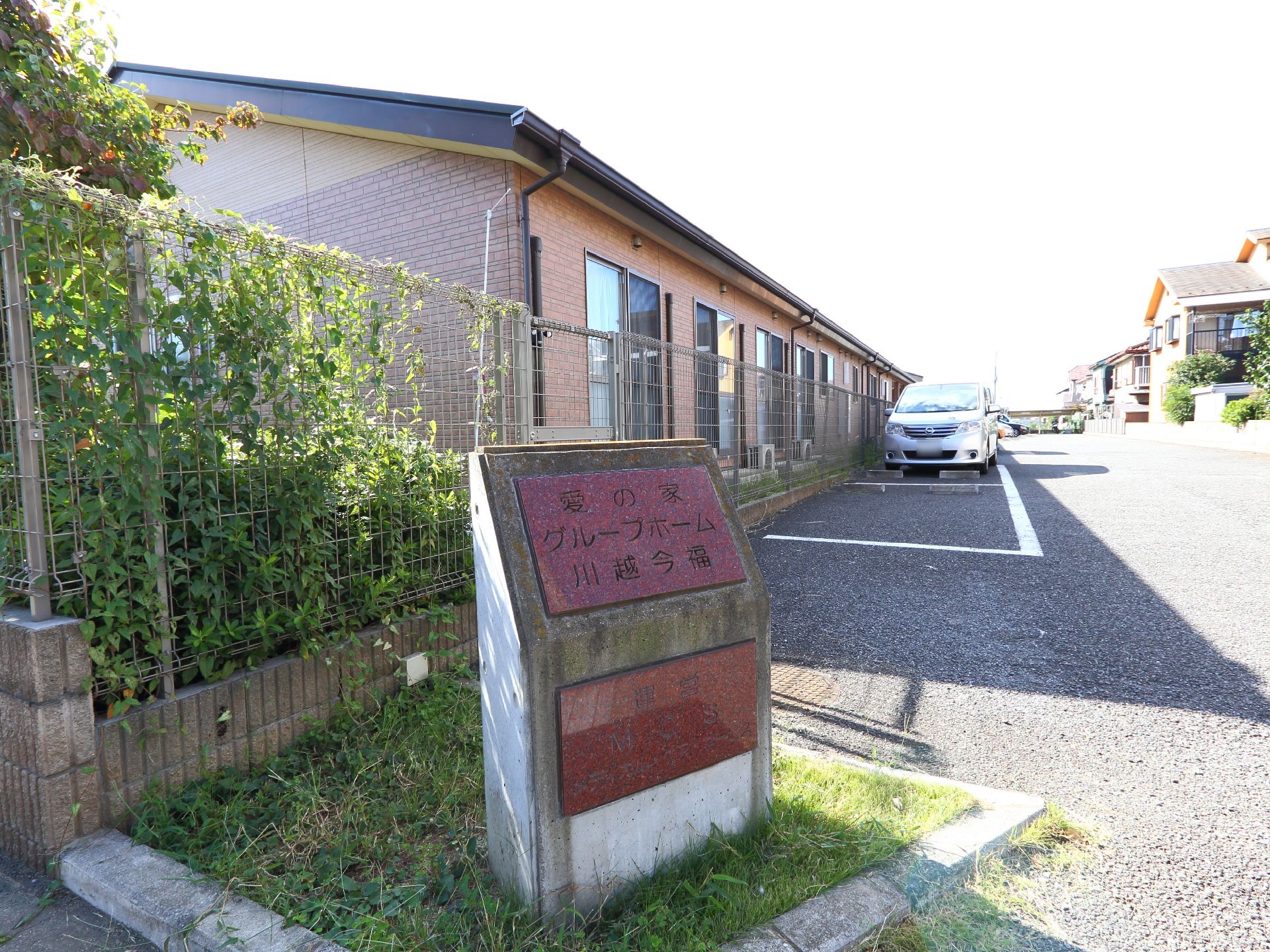 施設の駐車場の手前には施設名の入った石が設けられている。周囲は静かな住宅街で、近隣の住民とコミュニケーションが図れる。