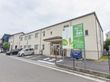 施設手前左側には駐車場あり。玄関の右側には自動販売機が置かれている。フェンスには施設の案内が書かれた看板が取り付けられている。