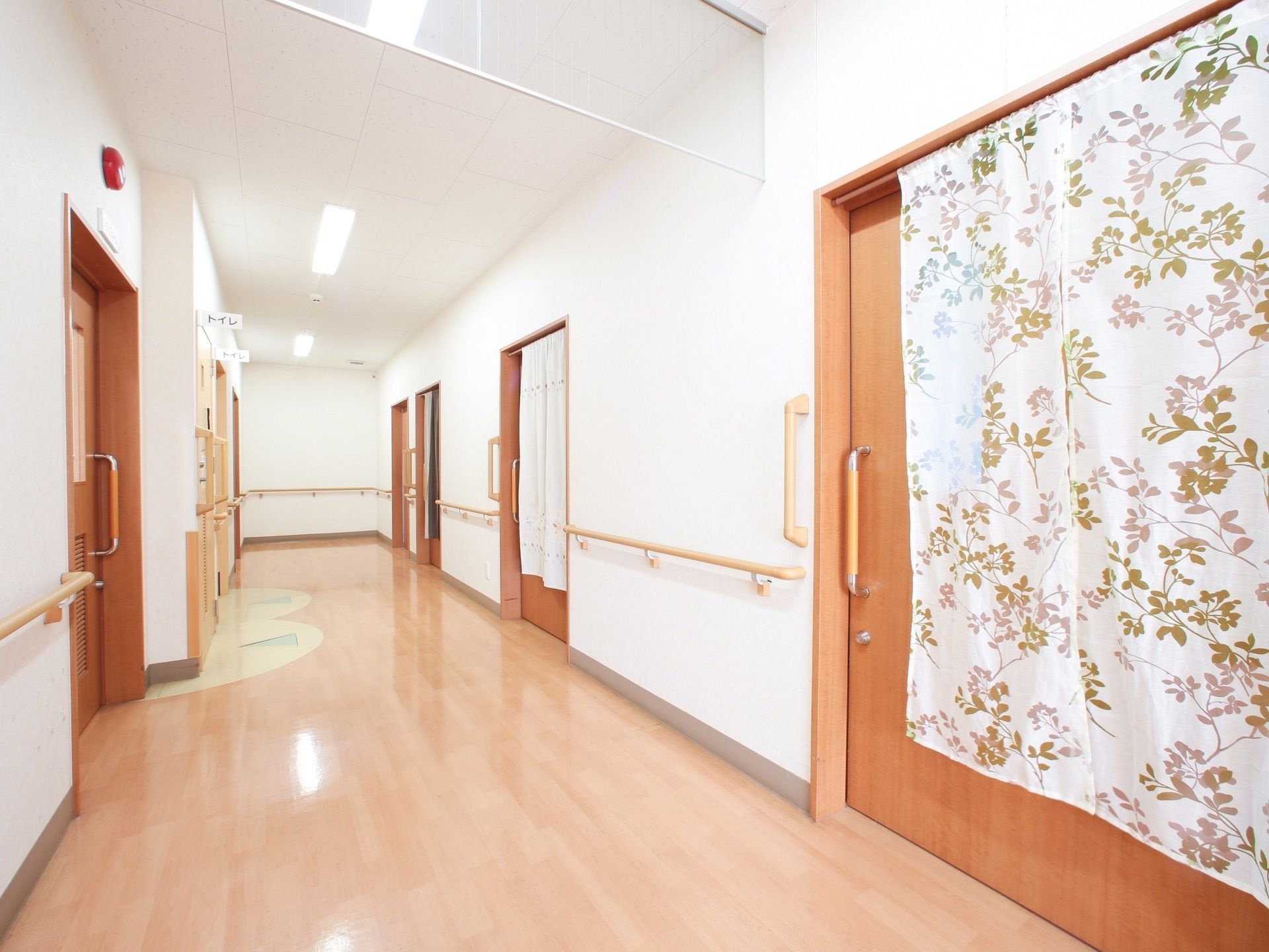 白いフローリングが使われた明るい床。両側の壁には手すりがついており、扉の前にはカーテンが掛けられている。