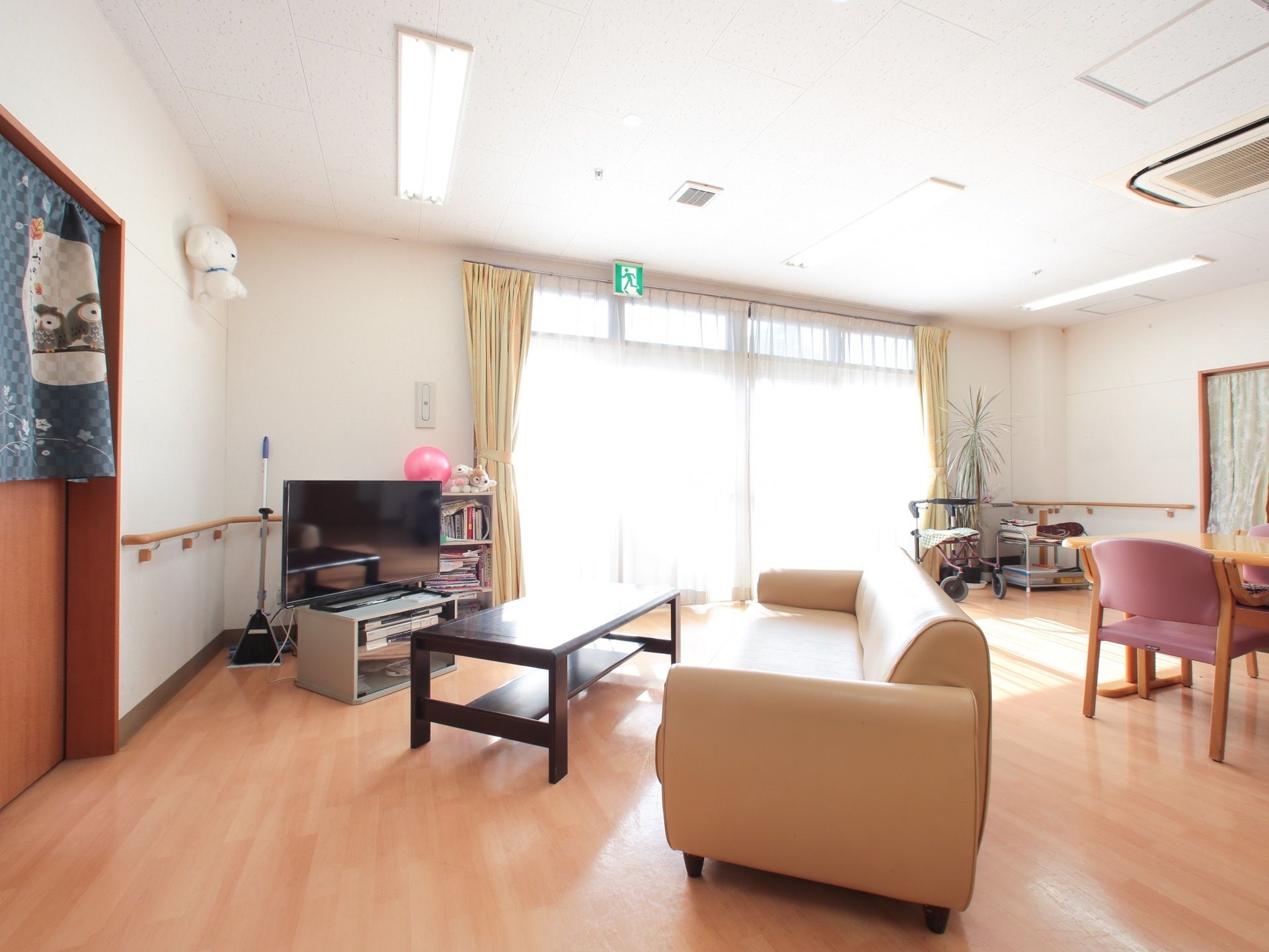 大きな窓がある広いホールに、テレビやソファ、本棚が置かれている。部屋のもう一方にはダイニングテーブルが置かれている。