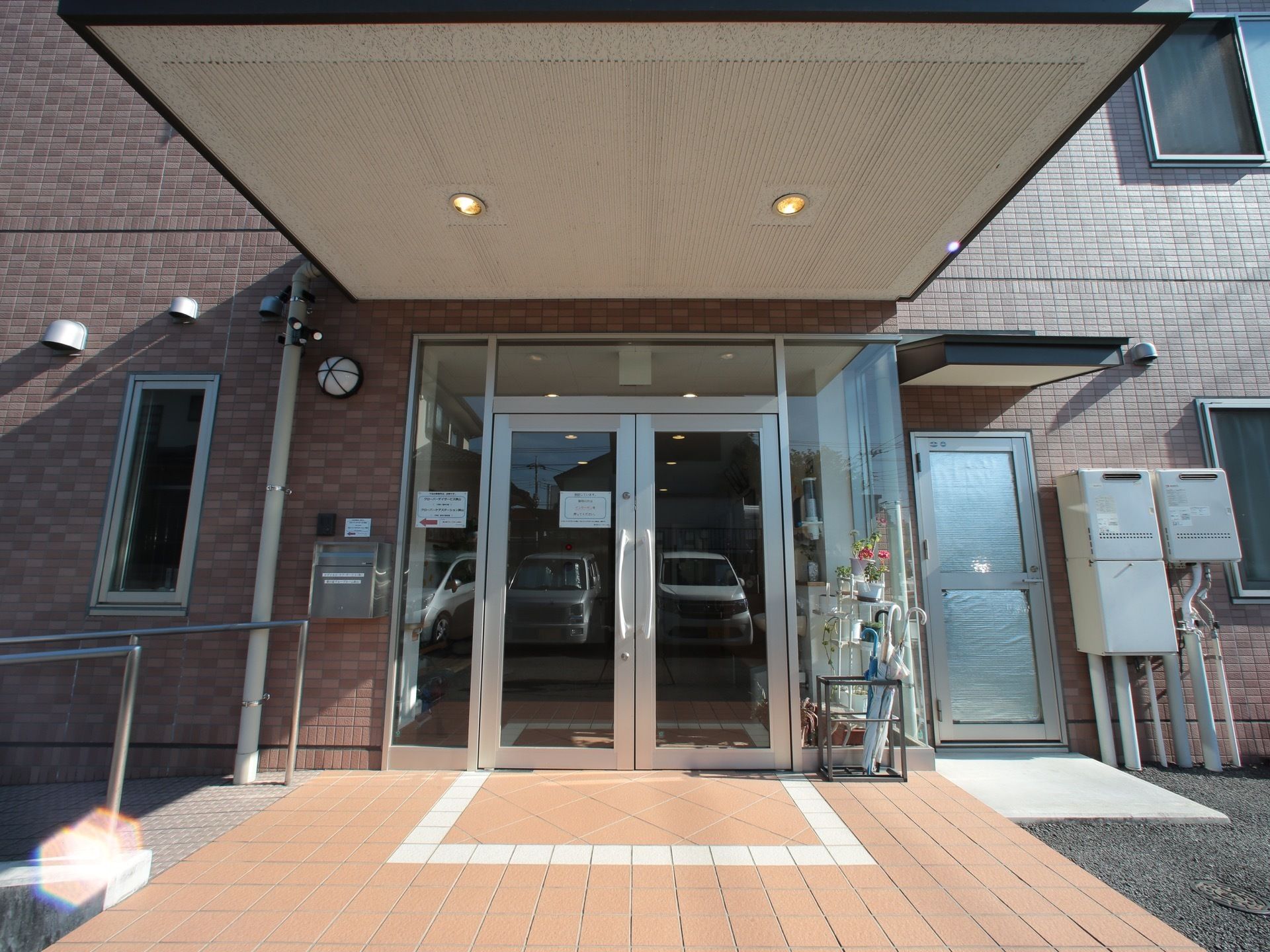 玄関扉はガラス戸になっているので、中の様子を見ることが出来る。外には傘立てがあり、傘が数本いれられている。