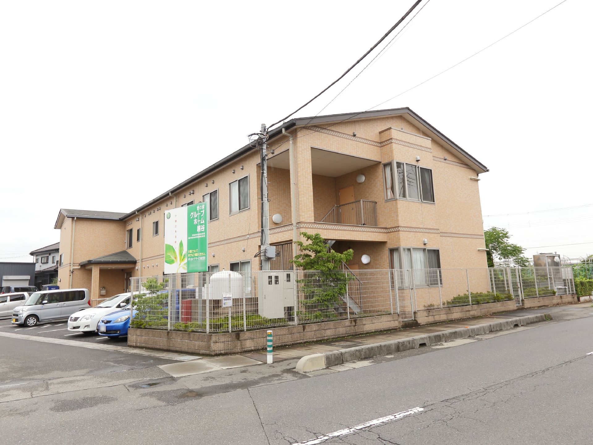 田畑などの自然の中にあるベージュ色のホーム。大きな看板が掛かっているので見付けやすい。駐車場も設けられている。