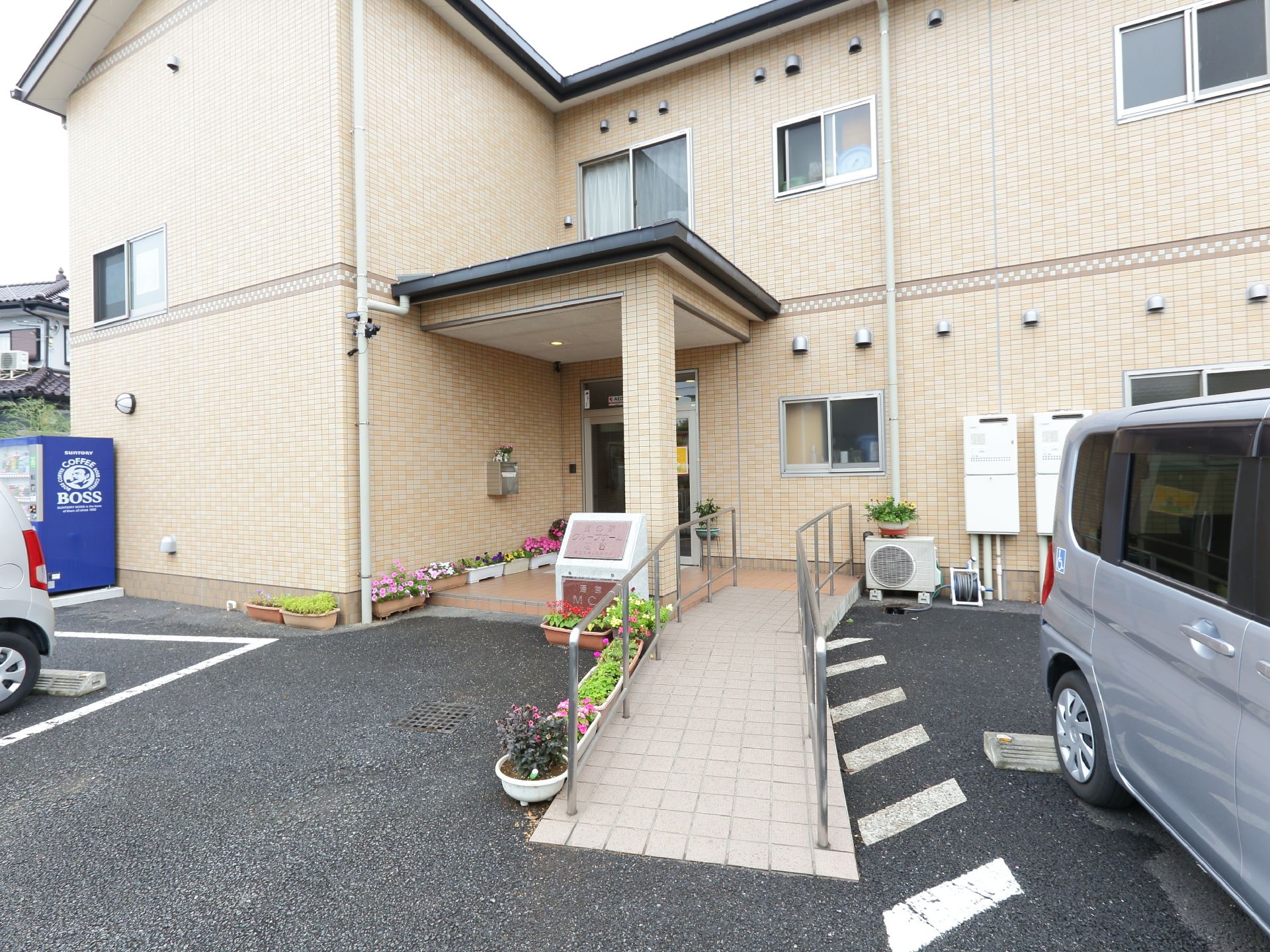 玄関前には幅の広いスロープと手すりが設置されている。庇が付いており、雨の日も慌てる必要がない。目の保養になるプランターの花が置かれている。