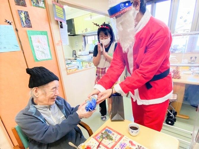 サンタクロースとトナカイに扮したスタッフからプレゼントを受け取るシニア女性