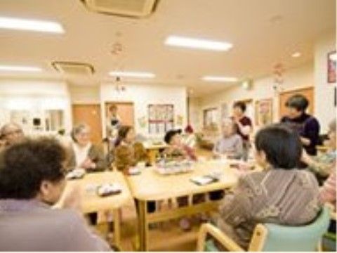テーブルを囲んで座る入居者とそこに向かって説明を行うスタッフ