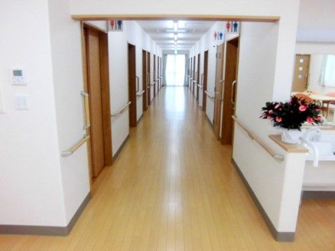 まっすぐ伸びたフローリングの廊下は、壁沿いに手すりが付いていて、トイレは３か所にある。突き当たりの大きな窓からは明るい日差しが入っている。
