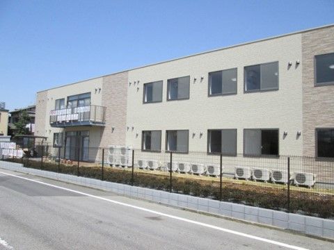 道路沿いに建つ長方形の２階建てで、壁はベージュ系基調で薄い茶色がアクセントになっている。日当たり良好な建物で、２階の一角にはベランダがある。