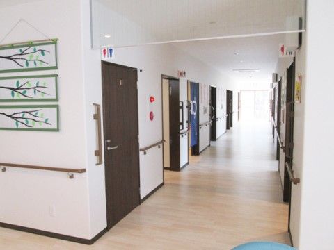 廊下は薄いベージュのフローリングで、幅が広いのですれ違いもスムーズに行える。トイレ表示が分かりやすく付いており、壁沿い全てに手すりがある。