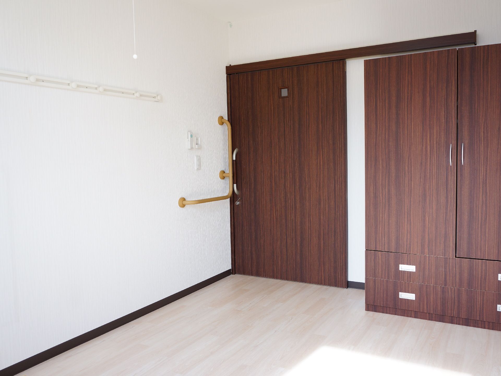 大きなクローゼットがある。ドアの近くには手すりがついている。木目調と白の壁が落ち着いた雰囲気である。