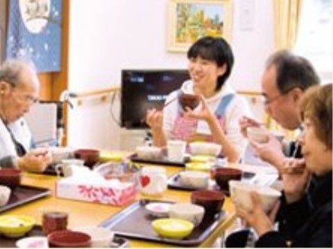 食卓を挟んでシニア男性に笑顔で話しかける女性スタッフ