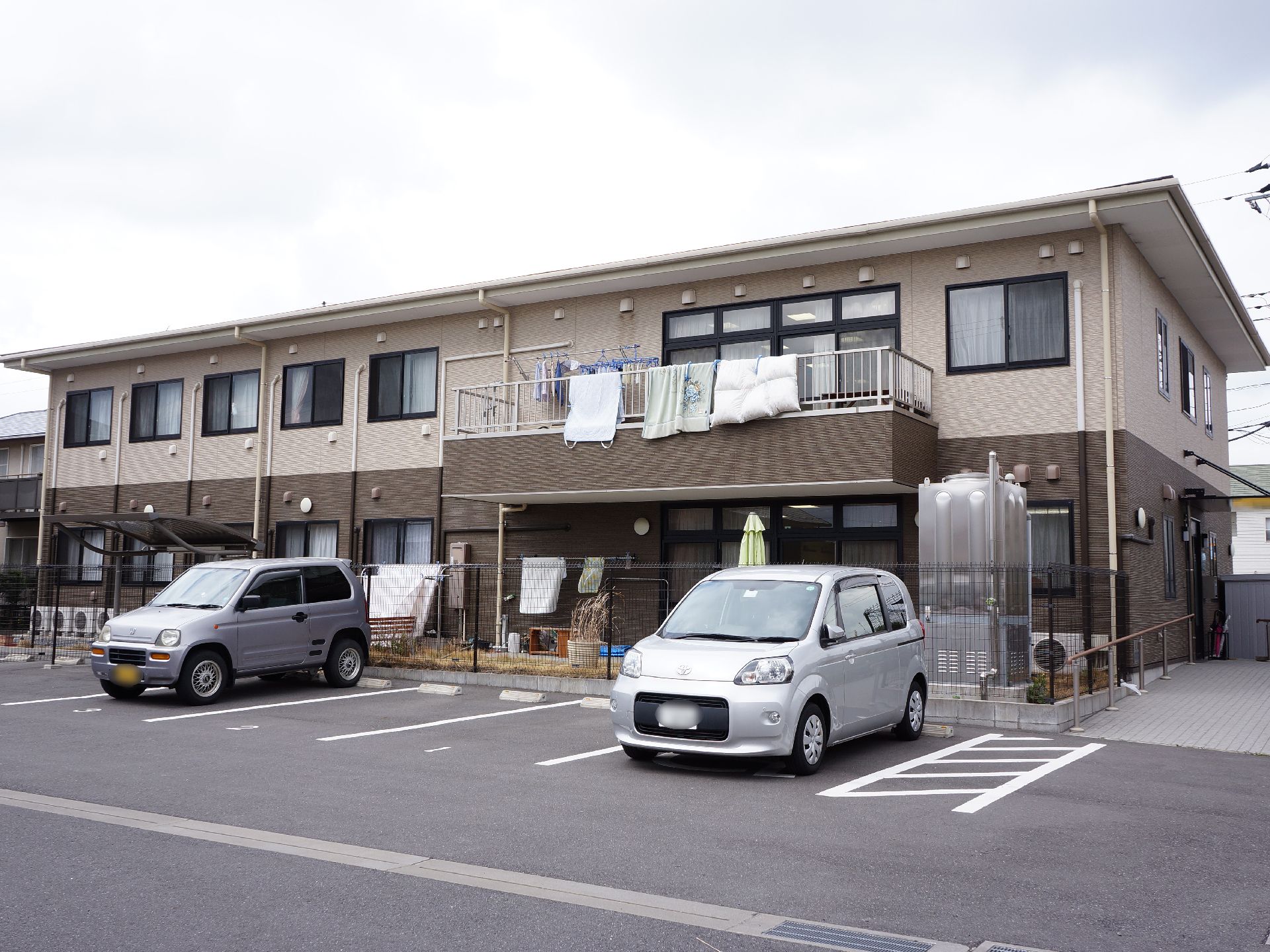 二階建ての建物で、一階部分と二階部分の壁の色が違っているデザイン。手前には駐車場があり、駐車場から玄関までは緩やかなスロープとなっている。