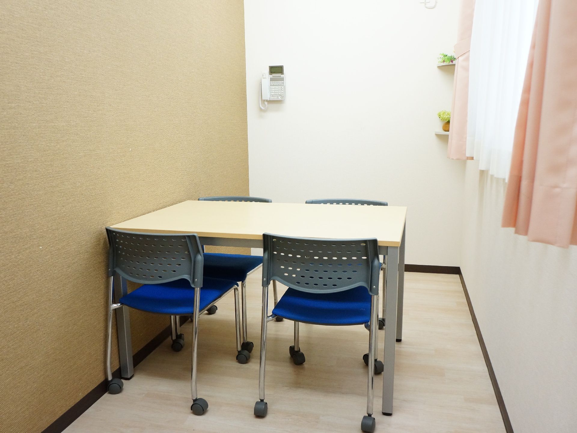 4人掛けのテーブルとイスが置かれた部屋。窓もあり、自然の光が入り明るい。壁には電話が設置されている。