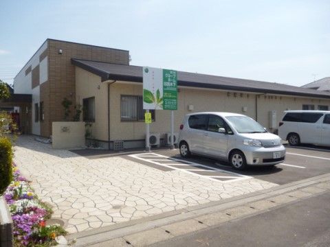 施設の入口へと続く通路は一直線に伸びており、通路沿いに鮮やかな色合いの草花が植えられている。通路の横には駐車スペースが整っている。
