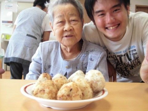 大皿に乗せたおにぎり越しに記念撮影を行うシニア女性と男性スタッフ