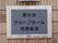 黒い文字で白い縁のグレーのプレートに施設名が書かれている。入口でどこの施設かわかるように表札がつけられている。