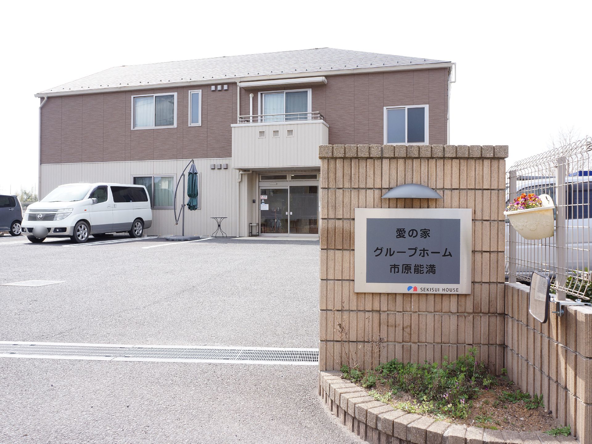 手作り感のあるレンガで作られた門柱には看板がかけてあり、外壁はツートンカラーになっている。施設の前は駐車場になっており、広々としている。