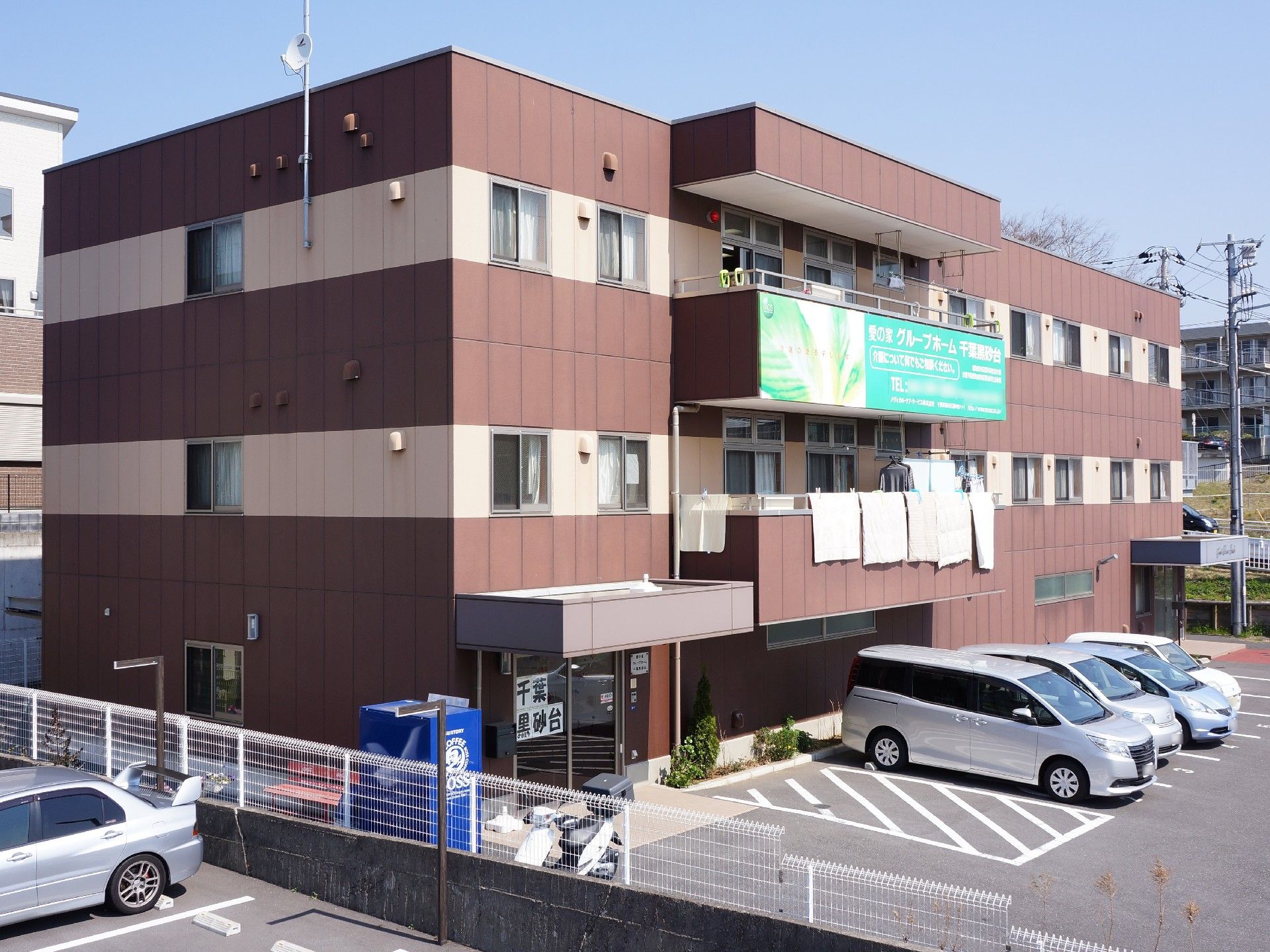 茶色い建物のある敷地内には、自動販売機が設置されている。駐車場は正面玄関の前に、優先駐車スペースがある。
