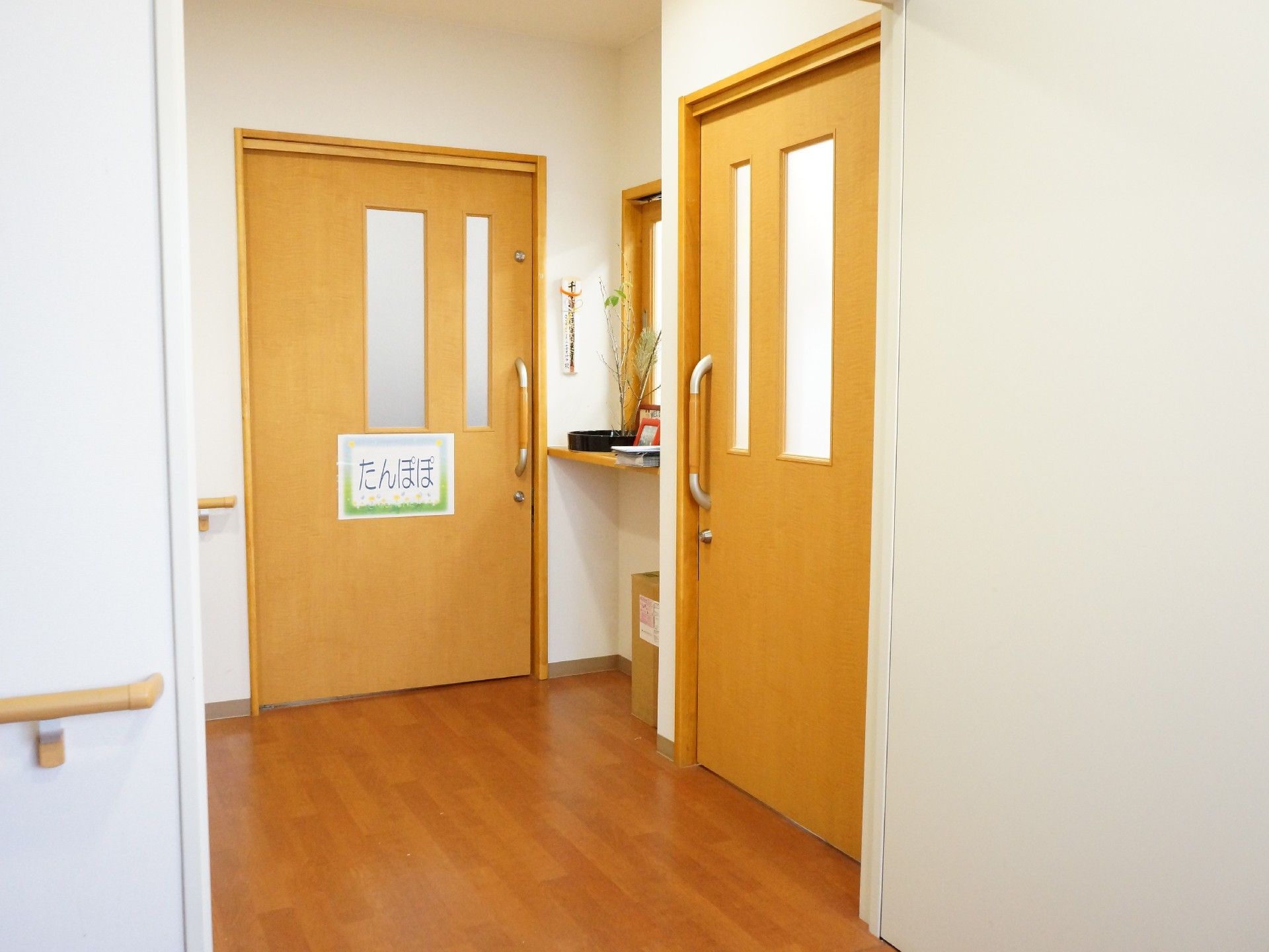 廊下の角の部屋のドアは大きな引き戸で、一つには「たんぽぽ」と書かれた紙が貼ってある。角には小さい受付窓とカウンターがある。