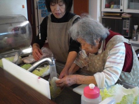 シンクで野菜を洗うシニア女性とそれをサポートするスタッフ
