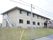 施設の外観である。2階建ての施設で、外壁はベージュで、落ち着いた印象である。1階の窓下には空調機の室外機がずらっと並んでいる。