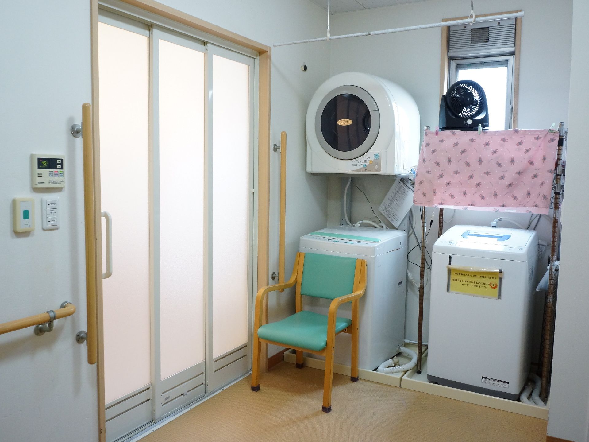 浴室前の脱衣スペース。洗濯機と乾燥機が置かれ、着替える際に使用できるよう、いすが置かれている。浴室への入り口は大きく開くスライド式である。