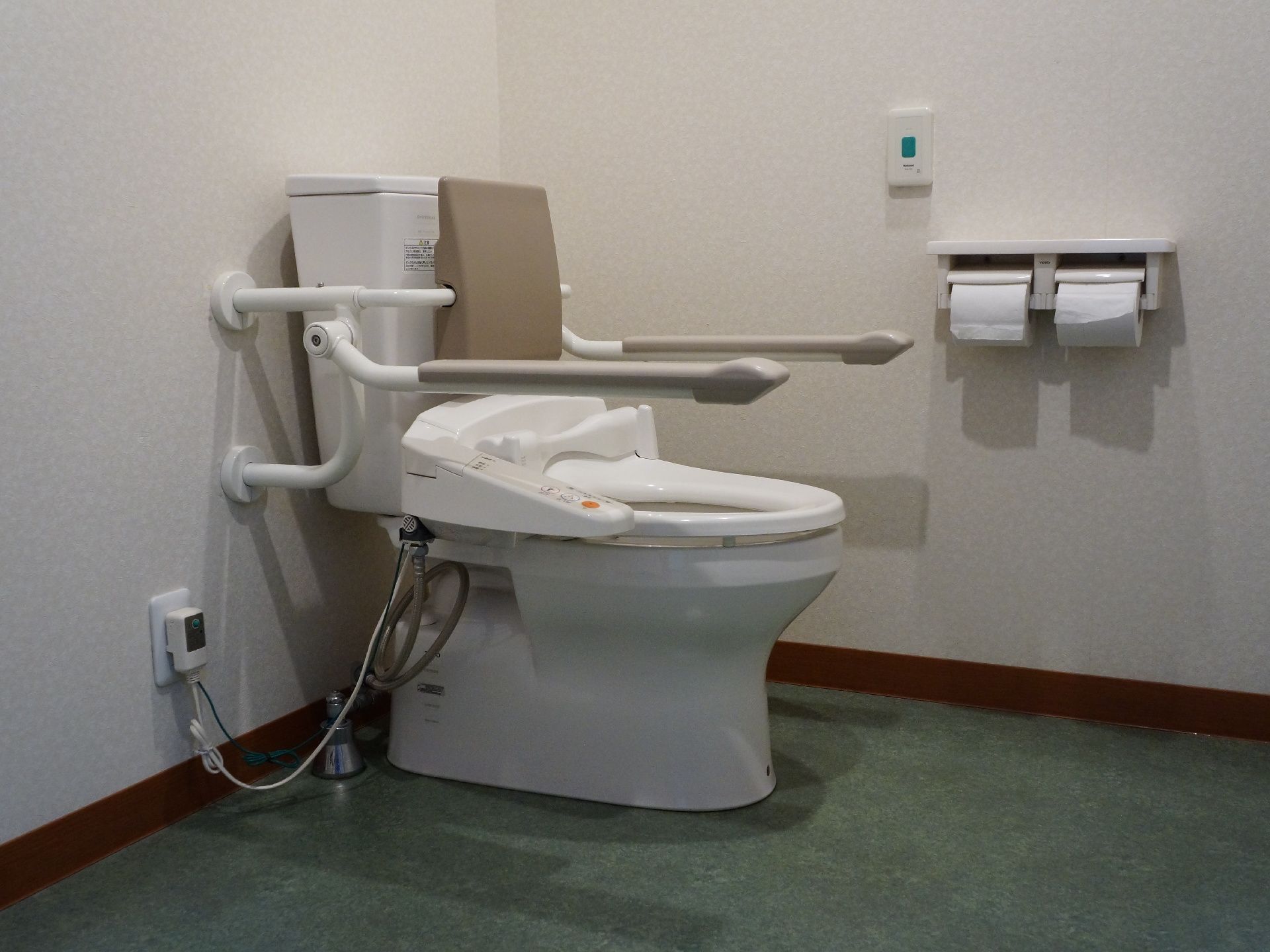 施設内の水洗トイレ。手すりや背もたれが設置され、安全に利用できるよう配慮されている。ペーパーホルダーのそばにはナースコールも設置されている。