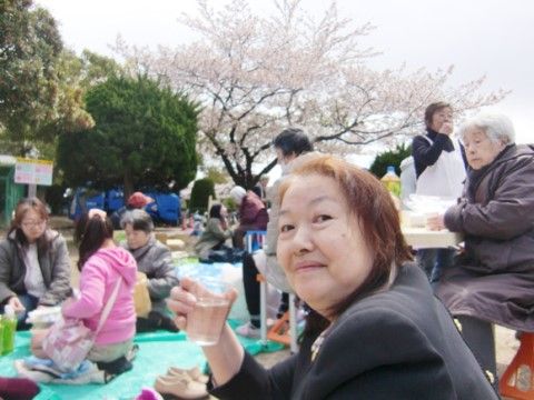 桜の咲いた公園でビニールシートを広げてお花見を楽しむ入居者