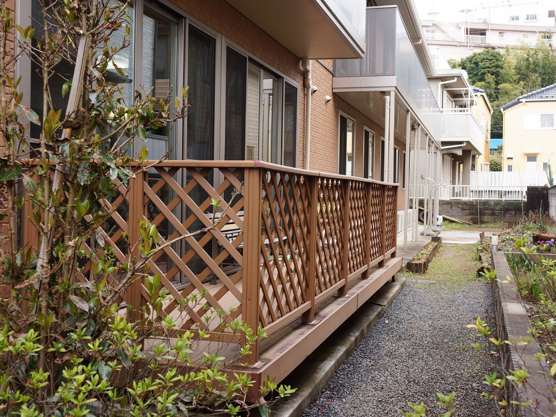通りと反対側の外観を外から見ると、2階と1階の1部にベランダが設置してある。敷地内に花壇があり、周りは住宅街である。