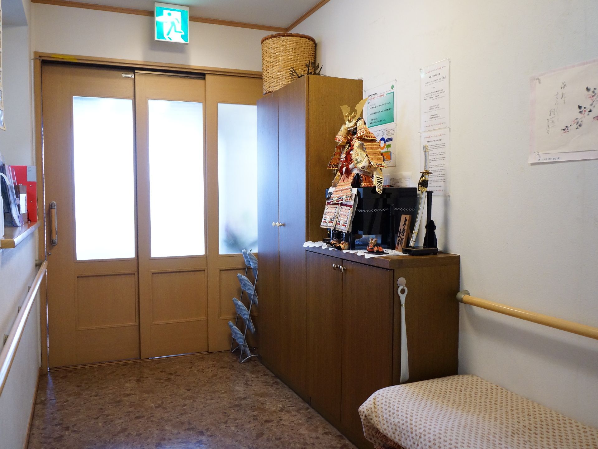 3つのスライドドアが設置された施設の玄関。横にはスリッパがかけられ、靴箱が並んでいる。その横には椅子が置かれている。