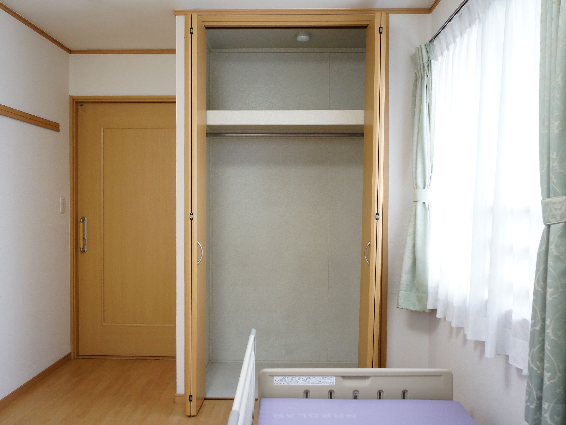 電動の介護用ベッドが置かれた明るい室内。入り口側には大きなクローゼットも造りつけられていて、様々なものを収納しておける。