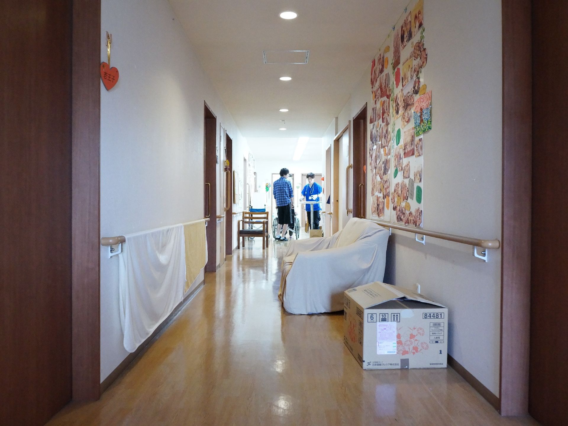 ゆとりのある幅の廊下にソファーとベンチがあり、先に広いスペースがある。部屋のドアの脇にネームプレートが付けられている。